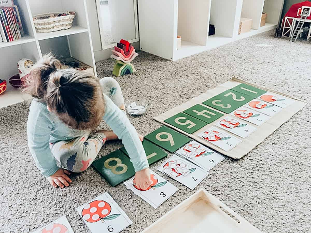 Дете подрежда образователни карти с цифри и илюстрации на ябълки за учене на броене.